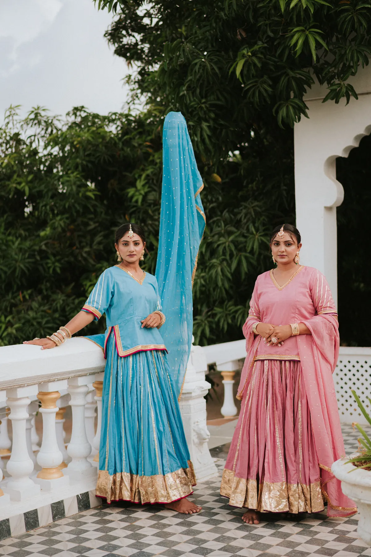 Two women in blue and pink traditional outfits posing on a white terrace
