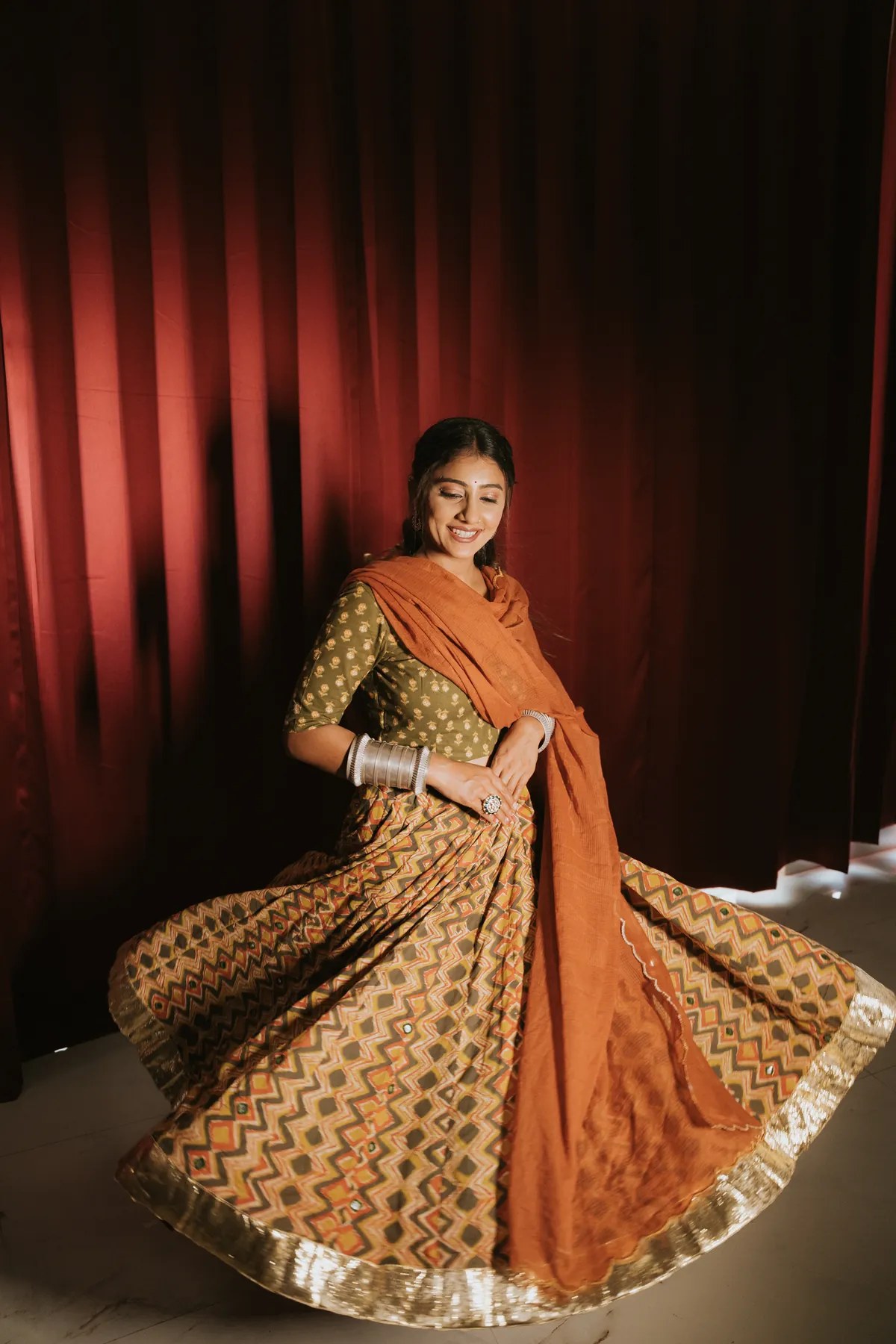 Woman twirling a patterned skirt in front of red curtains